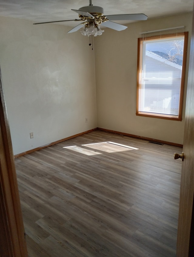 spare room featuring visible vents, baseboards, ceiling fan, and wood finished floors