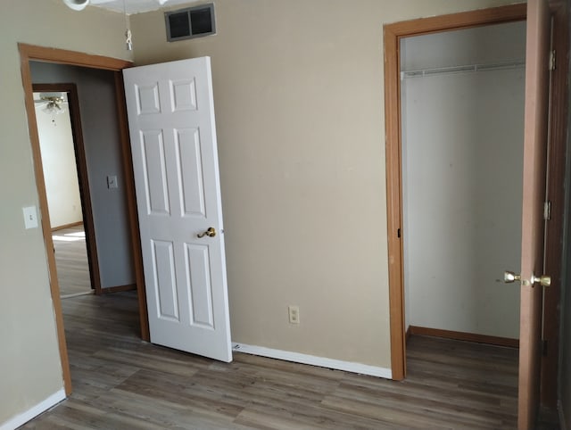 unfurnished bedroom featuring a closet, baseboards, visible vents, and wood finished floors