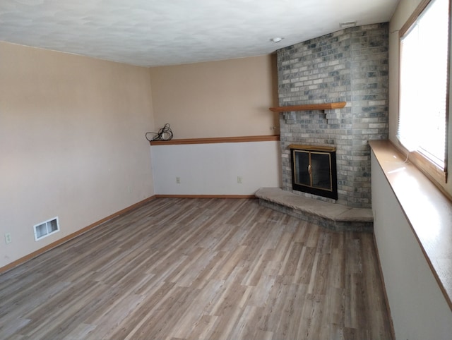 unfurnished living room with baseboards, visible vents, wood finished floors, and a fireplace
