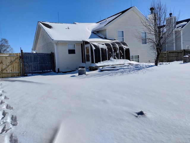 snow covered rear of property featuring a sunroom, a gate, and fence