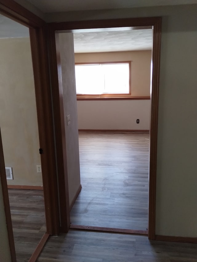 hall with visible vents, baseboards, and wood finished floors