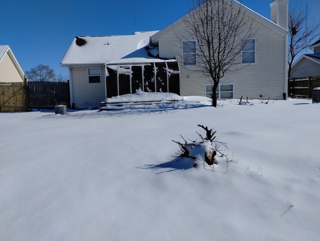 snow covered back of property featuring a chimney and fence
