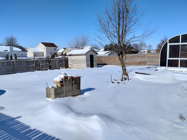 snowy yard with a fenced backyard, a residential view, a storage unit, and an outbuilding