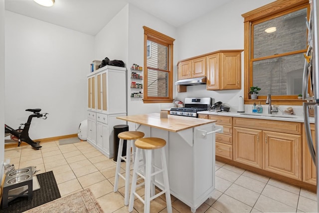 kitchen with butcher block countertops, under cabinet range hood, stainless steel gas range oven, a sink, and light tile patterned floors
