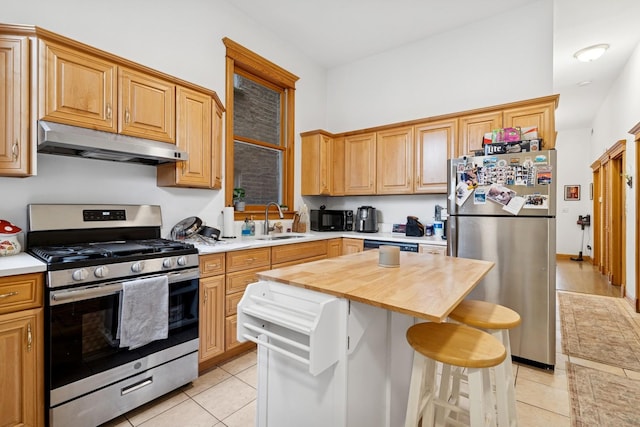 kitchen with a sink, a kitchen breakfast bar, butcher block counters, under cabinet range hood, and stainless steel appliances