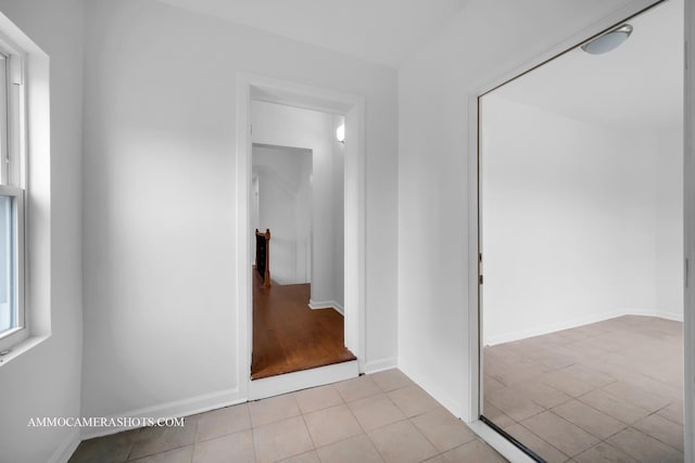 corridor with light tile patterned floors, baseboards, and an upstairs landing
