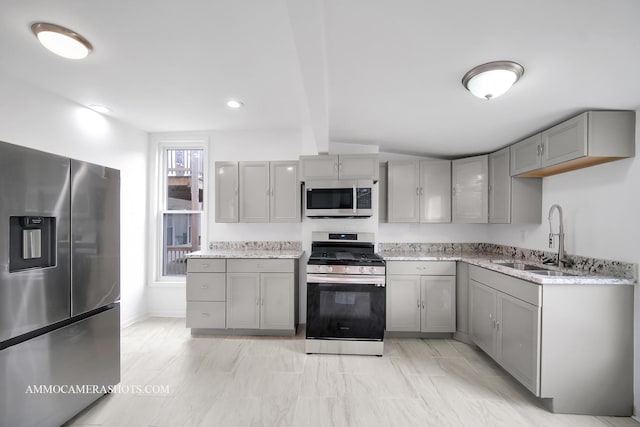 kitchen with a sink, stainless steel appliances, light stone counters, and gray cabinets