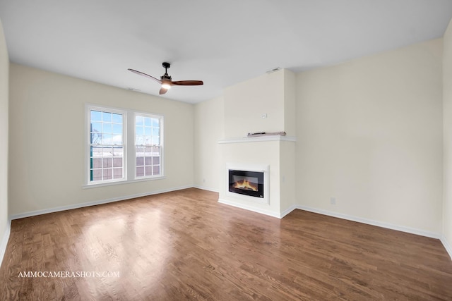 unfurnished living room with visible vents, baseboards, ceiling fan, wood finished floors, and a glass covered fireplace