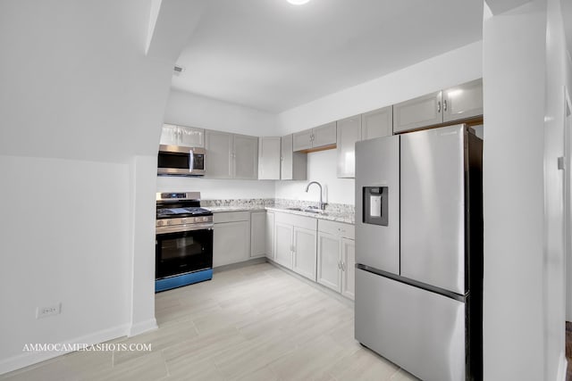 kitchen with light stone counters, gray cabinets, appliances with stainless steel finishes, and a sink