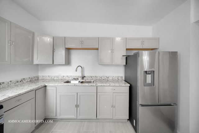kitchen with light stone counters, stainless steel fridge, gray cabinetry, and a sink