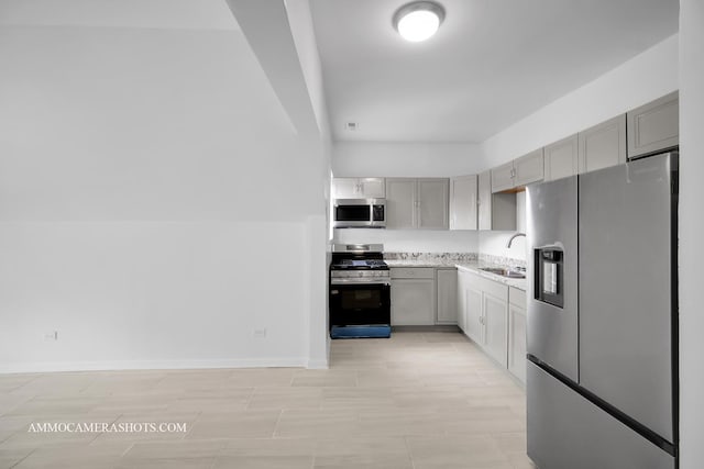 kitchen with gray cabinets, a sink, stainless steel appliances, light countertops, and baseboards