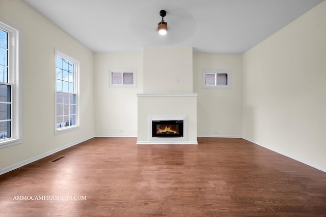unfurnished living room featuring visible vents, wood finished floors, baseboards, and a glass covered fireplace