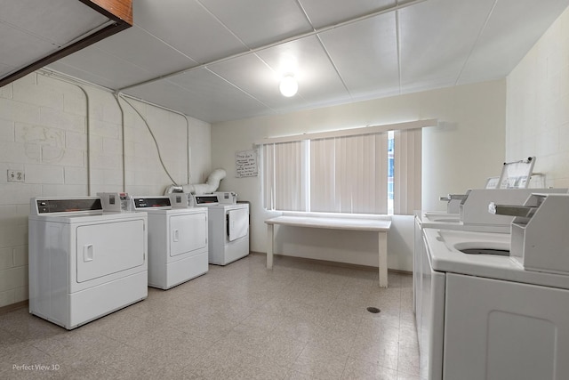 shared laundry area featuring light floors, washing machine and dryer, and concrete block wall