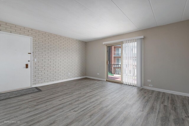 unfurnished room with baseboards, wood finished floors, and brick wall