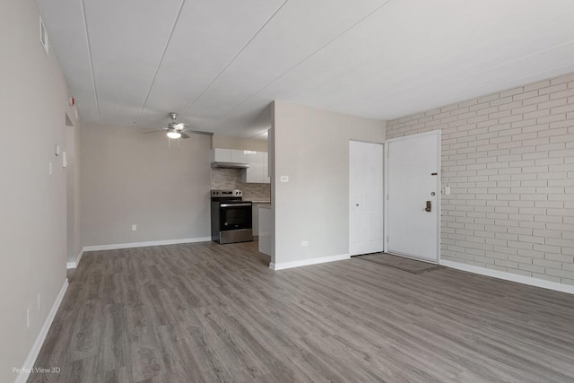 unfurnished living room featuring wood finished floors, a ceiling fan, baseboards, and brick wall