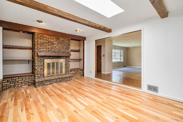 2201 W Acres Rd, Joliet, IL 60435 - unfurnished living room featuring beamed ceiling, wood finished floors, a brick fireplace, a skylight, and baseboards