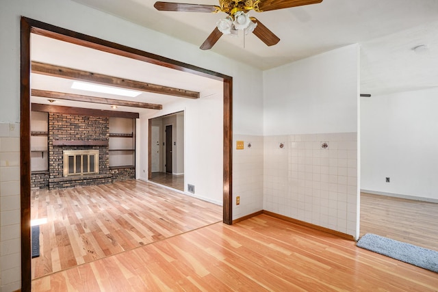 2201 W Acres Rd, Joliet, IL 60435 - unfurnished living room featuring light wood-type flooring, a fireplace, tile walls, a ceiling fan, and beamed ceiling