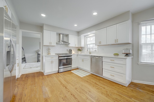 kitchen featuring decorative backsplash, light wood-type flooring, white cabinets, wall chimney exhaust hood, and appliances with stainless steel finishes