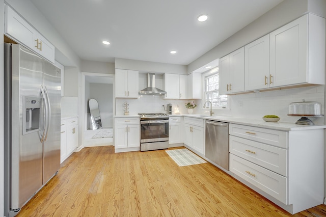 kitchen with wall chimney range hood, white cabinets, light countertops, backsplash, and appliances with stainless steel finishes