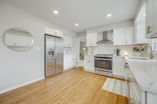 kitchen featuring stainless steel appliances, backsplash, wall chimney range hood, a sink, and light wood-type flooring