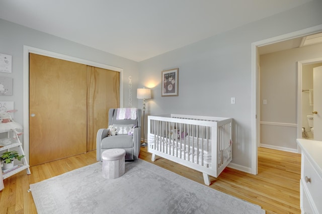 bedroom with a nursery area, a closet, light wood finished floors, and baseboards