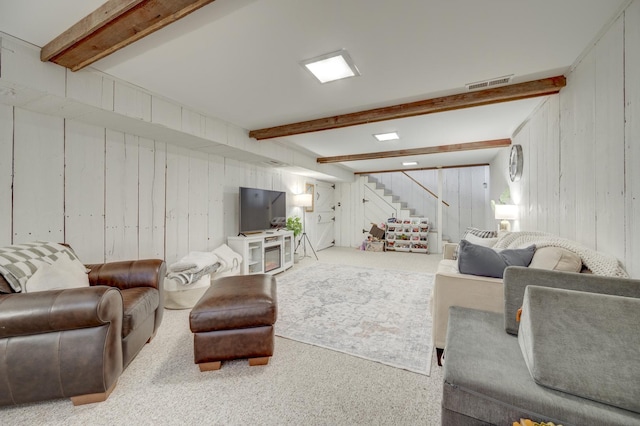 carpeted living room featuring wooden walls, visible vents, beam ceiling, and stairs