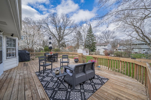 wooden deck with a shed, outdoor dining space, a grill, an outbuilding, and a residential view
