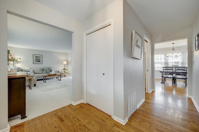 hall featuring baseboards, a notable chandelier, wood finished floors, and visible vents