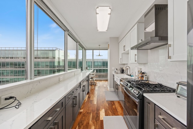 kitchen with wood finished floors, gas stove, a sink, wall chimney exhaust hood, and tasteful backsplash
