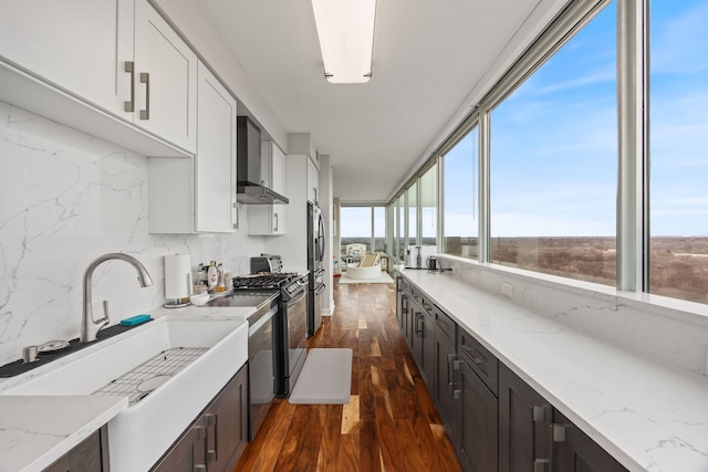 kitchen with a sink, dark wood-style floors, wall chimney exhaust hood, decorative backsplash, and stainless steel gas range