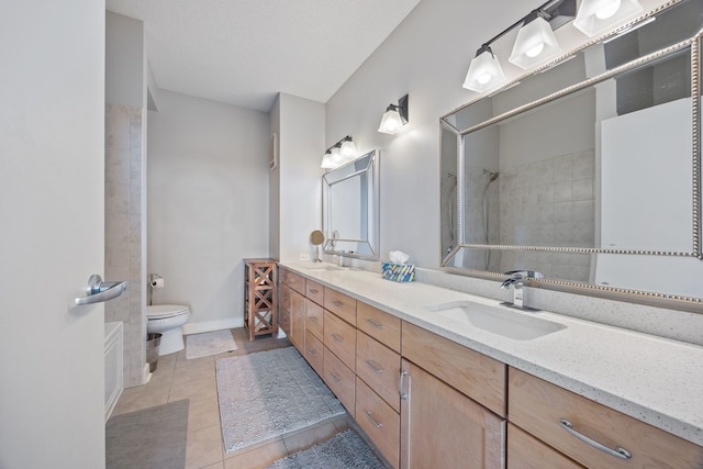full bathroom featuring double vanity, a tile shower, a sink, tile patterned floors, and toilet