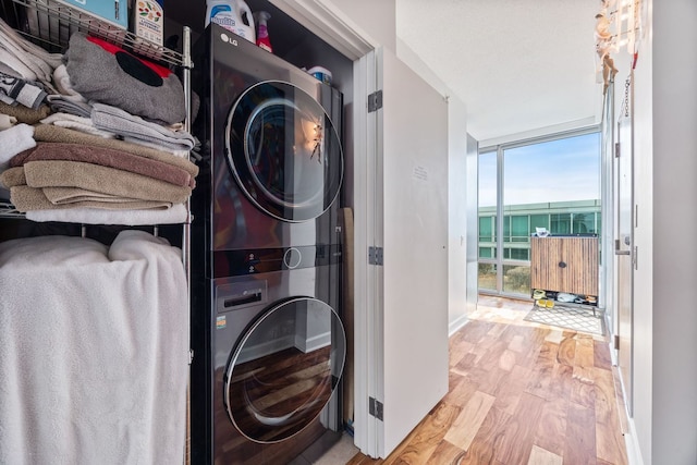 clothes washing area featuring laundry area, stacked washer and dryer, wood finished floors, and baseboards