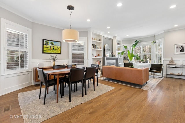 dining space with a fireplace, ornamental molding, visible vents, wood finished floors, and wainscoting
