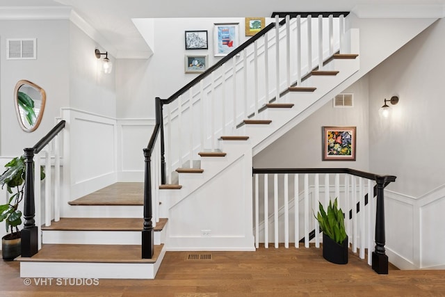 stairway with a decorative wall, visible vents, and wood finished floors