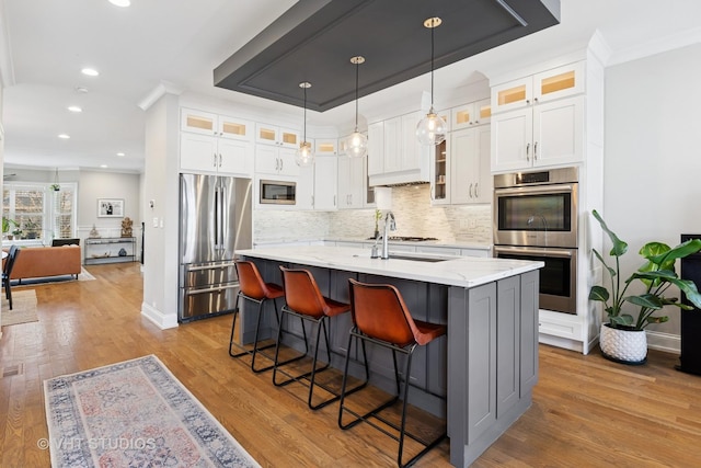 kitchen featuring white cabinets, appliances with stainless steel finishes, a kitchen island with sink, wood finished floors, and backsplash