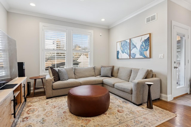 living room featuring light wood-style floors, visible vents, baseboards, and ornamental molding