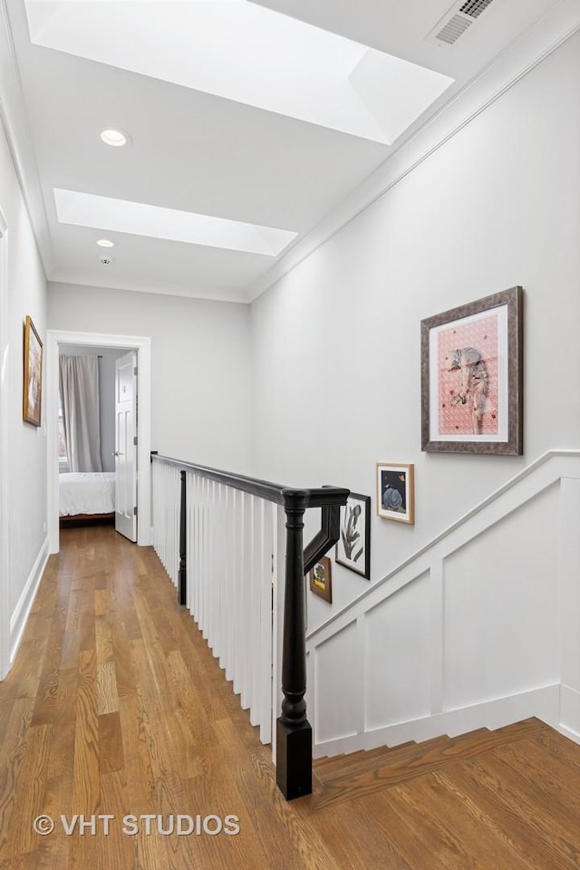 corridor with a skylight, a decorative wall, visible vents, and an upstairs landing