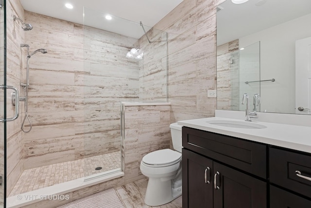 bathroom with tile walls, toilet, a stall shower, and vanity