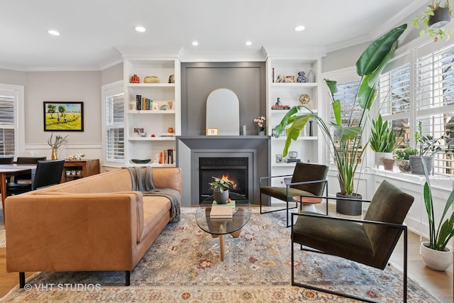 living area with a large fireplace, ornamental molding, recessed lighting, built in shelves, and wood finished floors