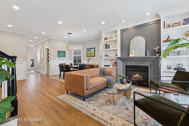living area with a warm lit fireplace, a wainscoted wall, light wood finished floors, and crown molding