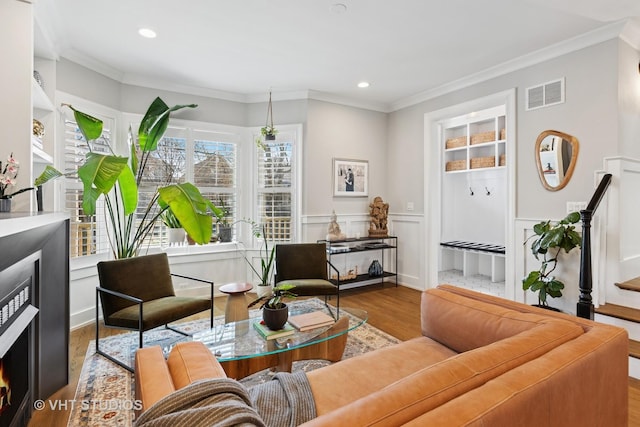 living room featuring wood finished floors, ornamental molding, visible vents, and a wainscoted wall