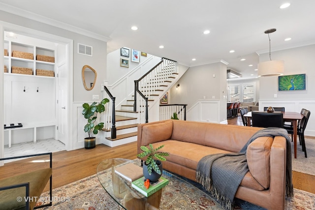 living area with crown molding, stairs, visible vents, a decorative wall, and wood finished floors