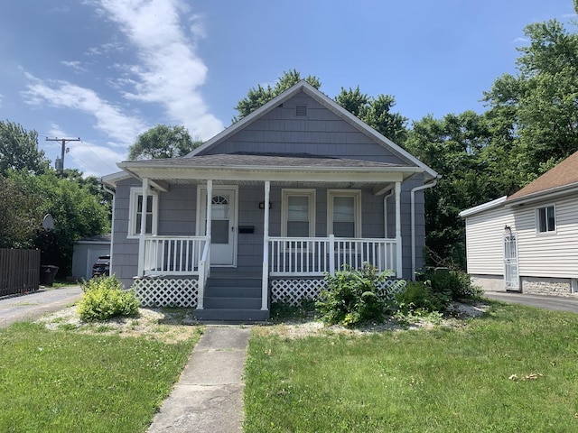 bungalow-style home with roof with shingles, covered porch, and a front lawn