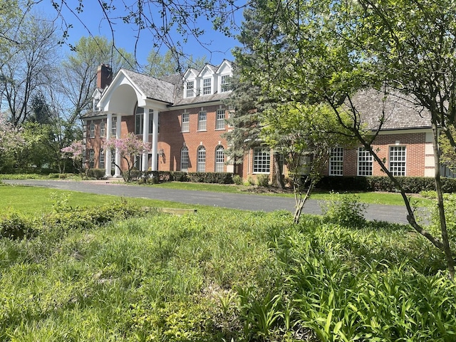 view of front facade featuring brick siding, a chimney, and a front lawn