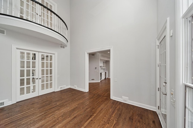 entrance foyer featuring baseboards, a towering ceiling, wood finished floors, and french doors