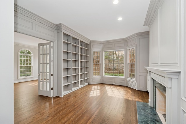 unfurnished living room featuring recessed lighting, ornamental molding, a decorative wall, a fireplace, and wood finished floors