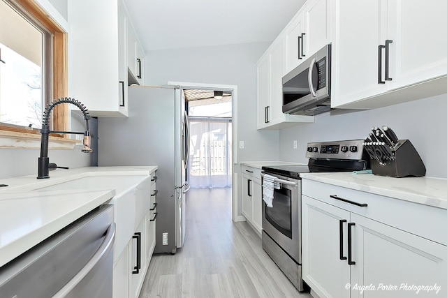 kitchen featuring white cabinetry, stainless steel appliances, light wood-style floors, and light stone countertops