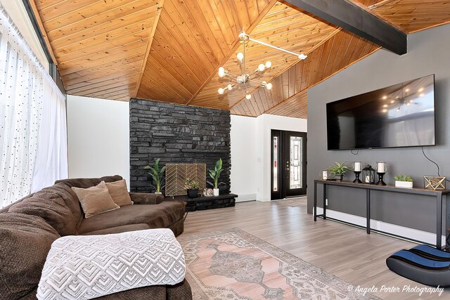 living area with wooden ceiling, wood finished floors, a stone fireplace, beamed ceiling, and an inviting chandelier