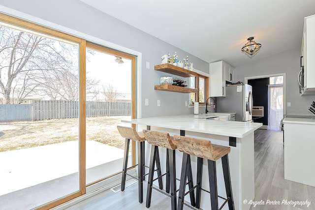 kitchen featuring light countertops, a peninsula, a breakfast bar, lofted ceiling, and white cabinetry