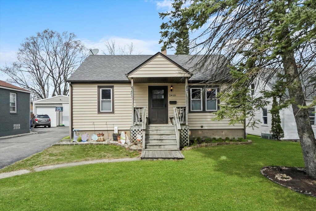 2410 W Ridgeland Ave, Waukegan, IL 60085 - bungalow-style home with an outdoor structure, cooling unit, a shingled roof, a front lawn, and a garage